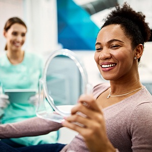 Patient smiling at reflection in handheld mirror next to dentist