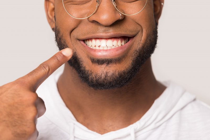 a young man pointing to his teeth and gums with only the lower half of his face showing