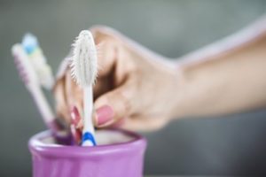 A hand reaching for a toothbrush with frayed bristles
