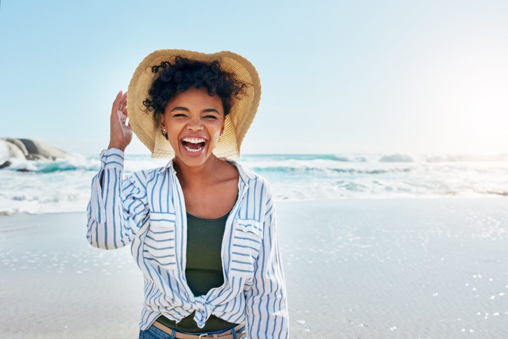 Smiling woman holding her hat while on the beach