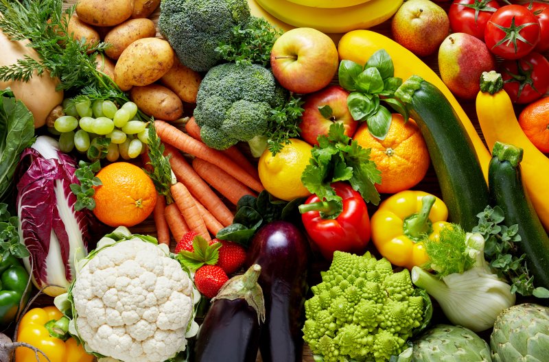 Various fresh produce of all colors, including but not limited to cabbage, cauliflower, bell peppers, cucumbers, apples, eggplants, grapes, and oranges
